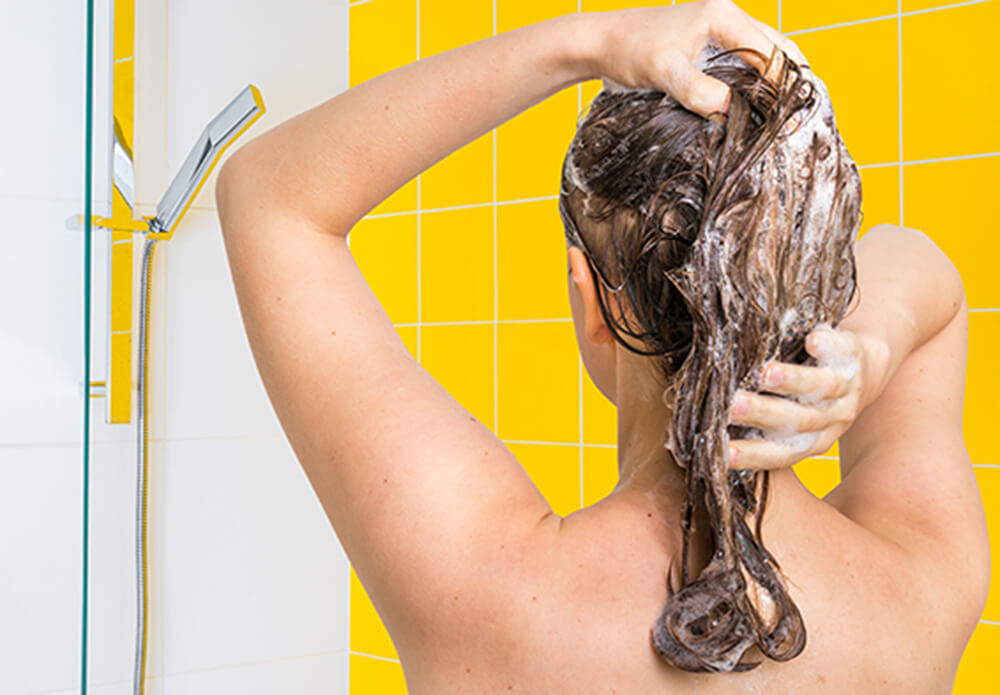Woman washing hair in shower with yellow tiles in background